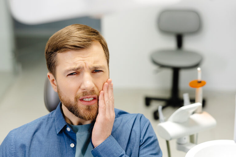 Sad Man Sitting In Dental Chair Suffering From Acute Tooth Pain,